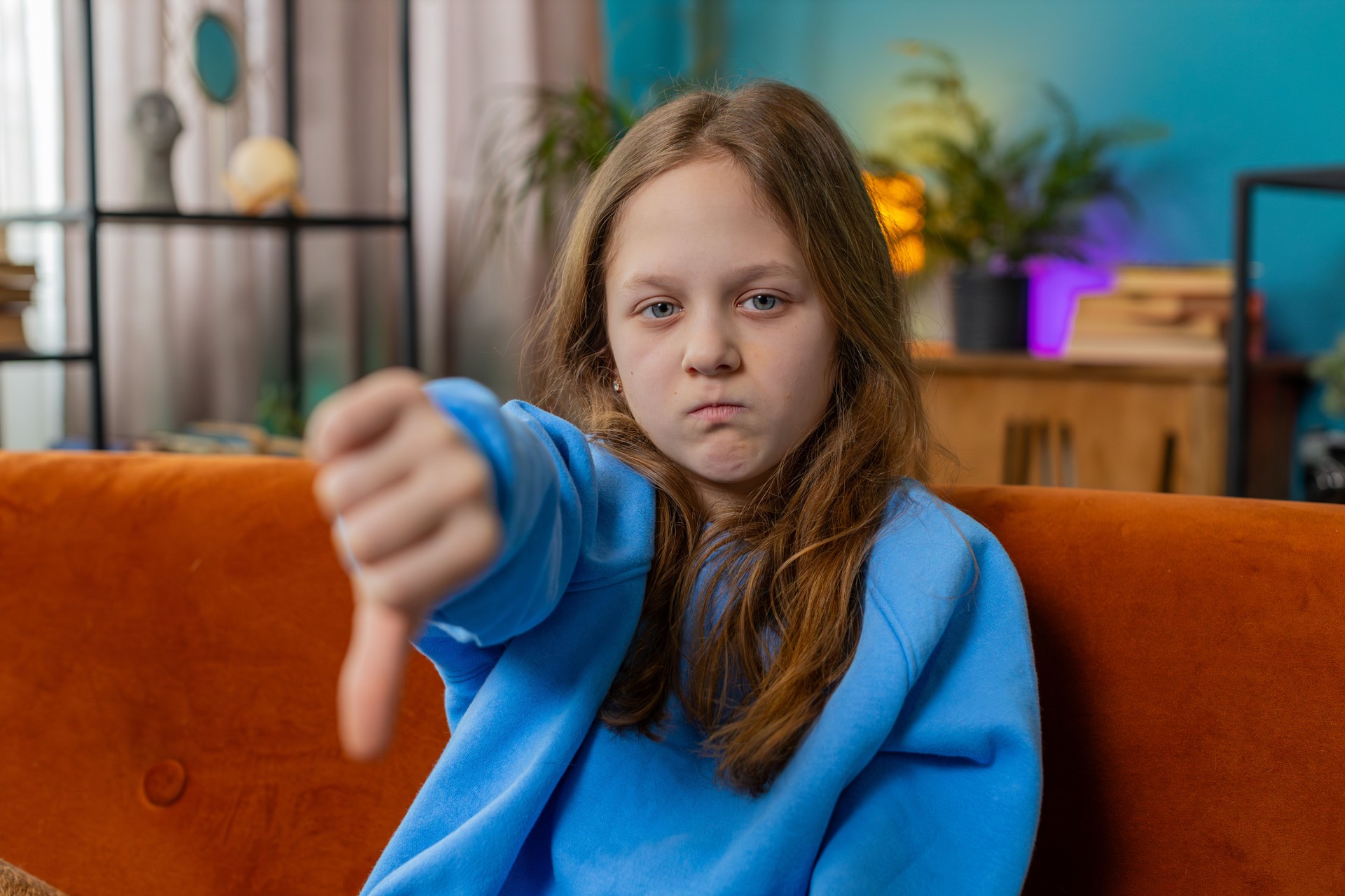 Upset teen girl showing thumbs down dislike bad work disapproval dissatisfied feedback at home